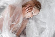 A peaceful woman with closed eyes lies wrapped in translucent plastic, symbolizing fragility and beauty.